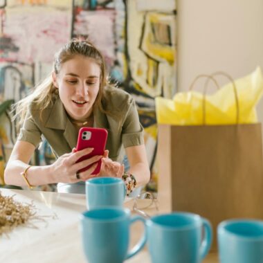 Woman using smartphone surrounded by cups and bag, ideal for online business themes.